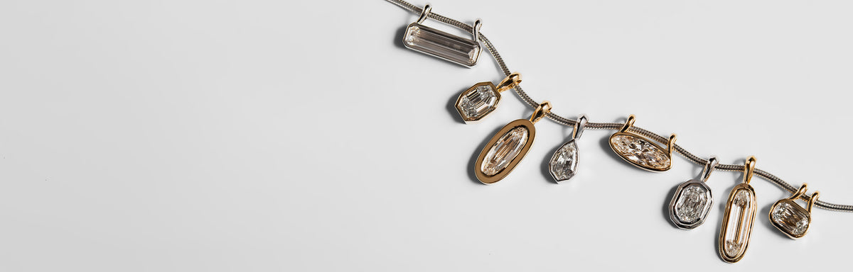 A close-up of a silver-toned snake chain with multiple architectural, unique-shaped diamond charms in gold and silver bezel settings, arranged diagonally on a white background.